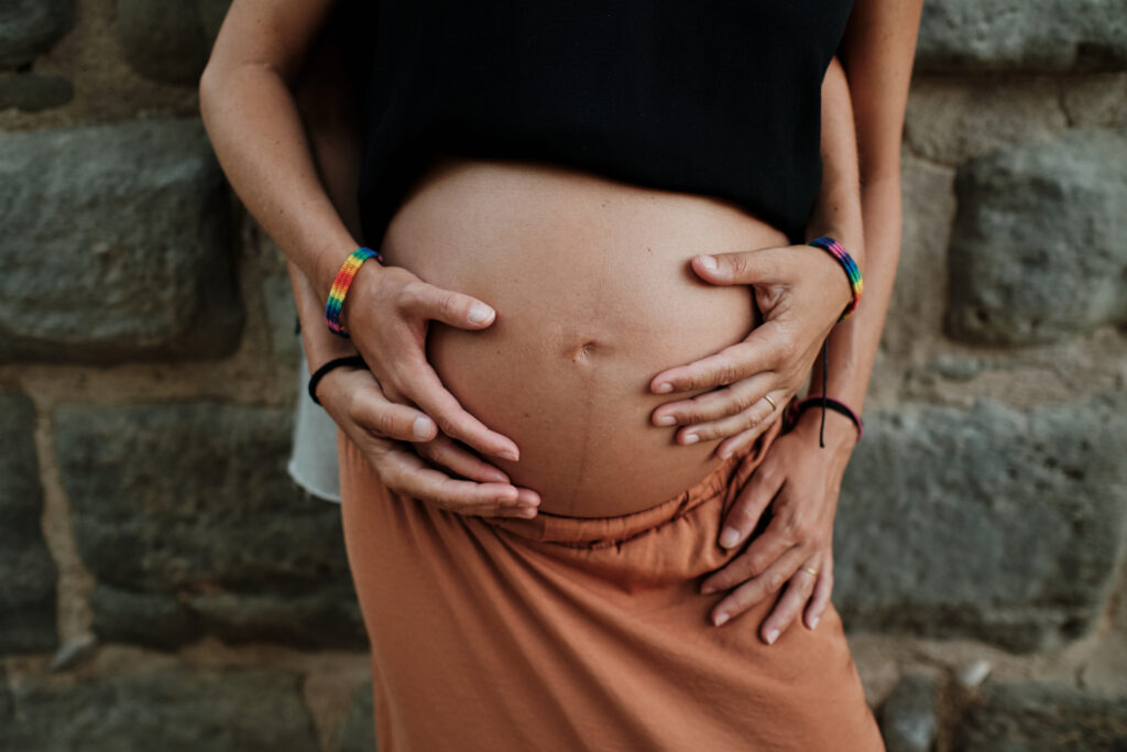 Closeup of a lesbian couple holding their belly bump in a park - pregnancy
