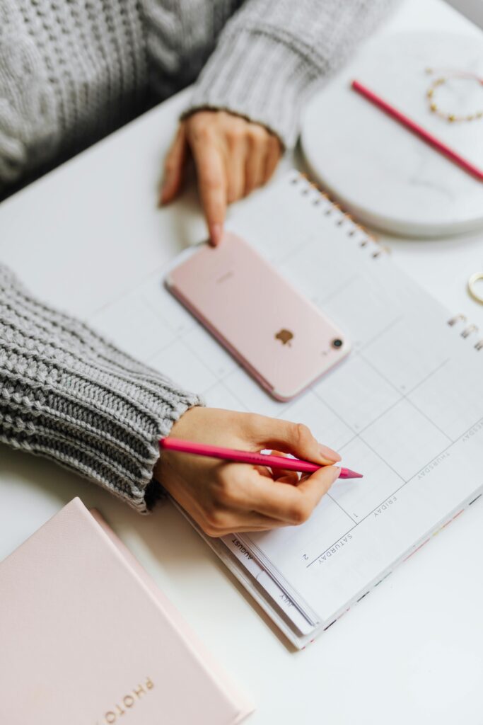 pexels-photo-14299948-14299948 Close-up of a woman planning on a calendar using a smartphone and pen.
