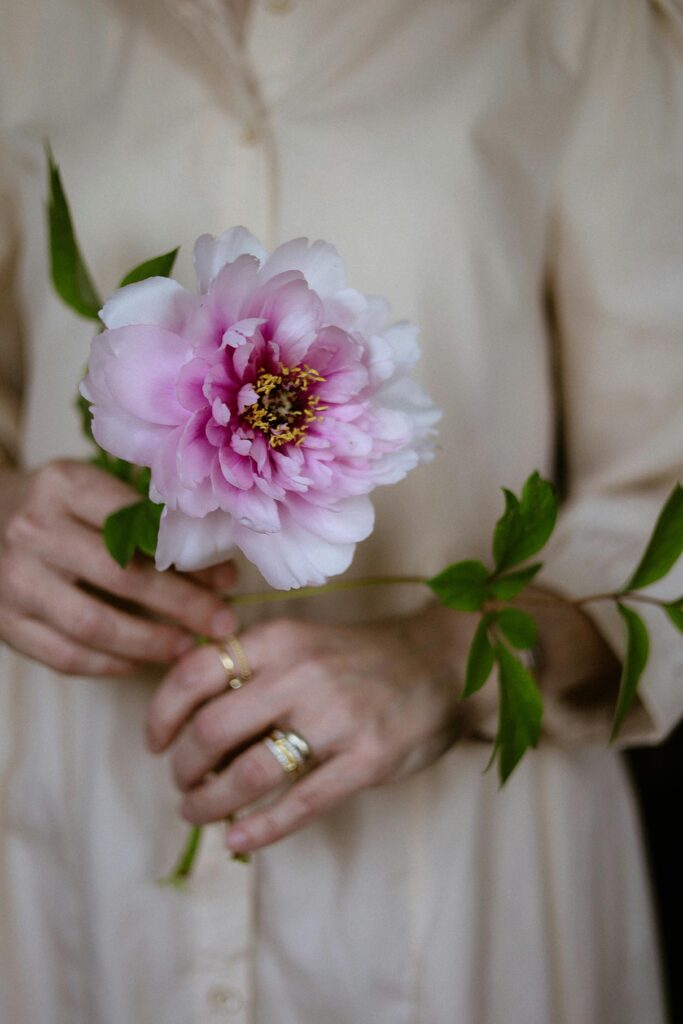 pexels-photo-31583567-31583567 Close-up of a woman holding a blossoming pink peony, showcasing elegance and simplicity.