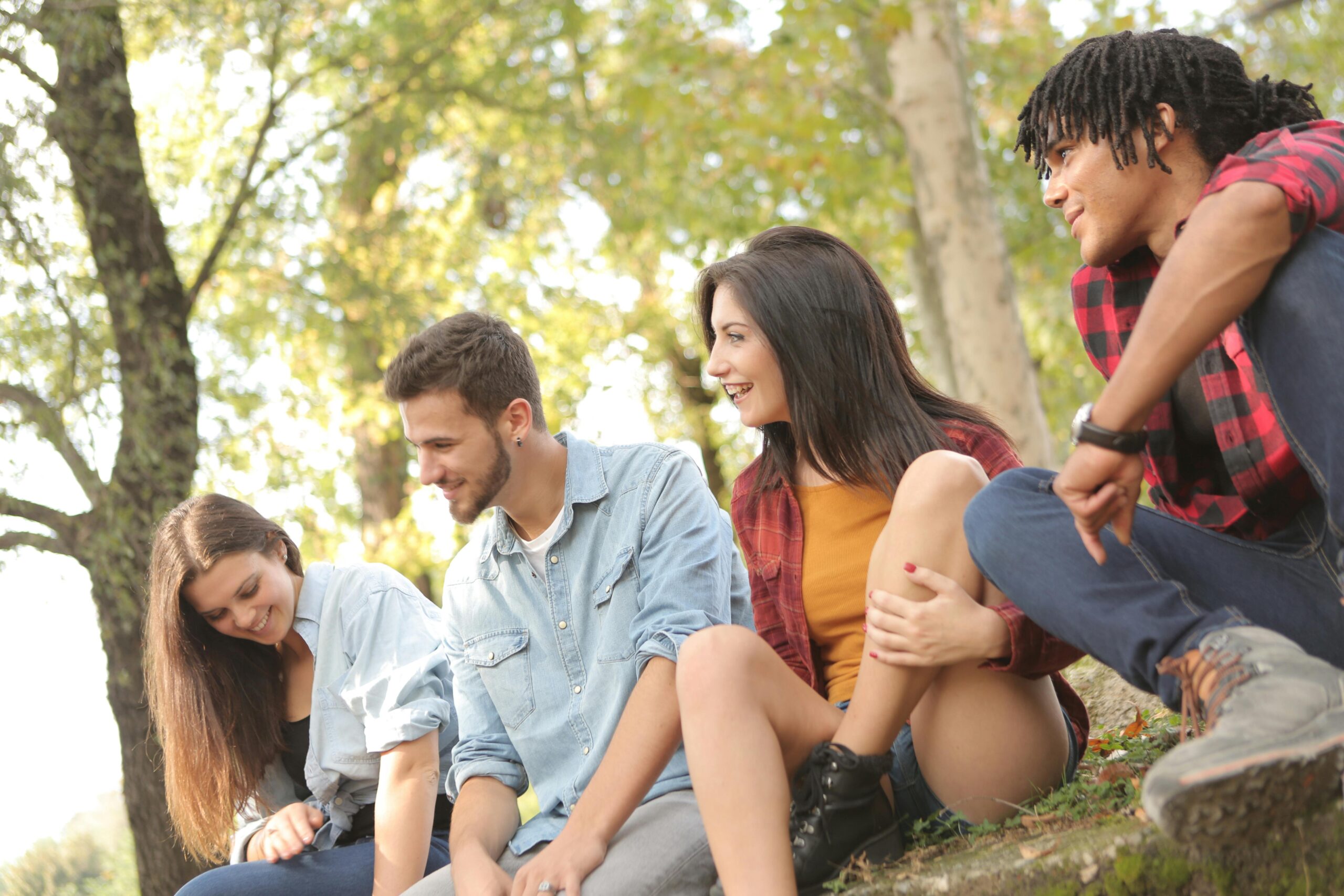 A multicultural group of friends enjoying a sunny day in the park, laughing and sitting together.